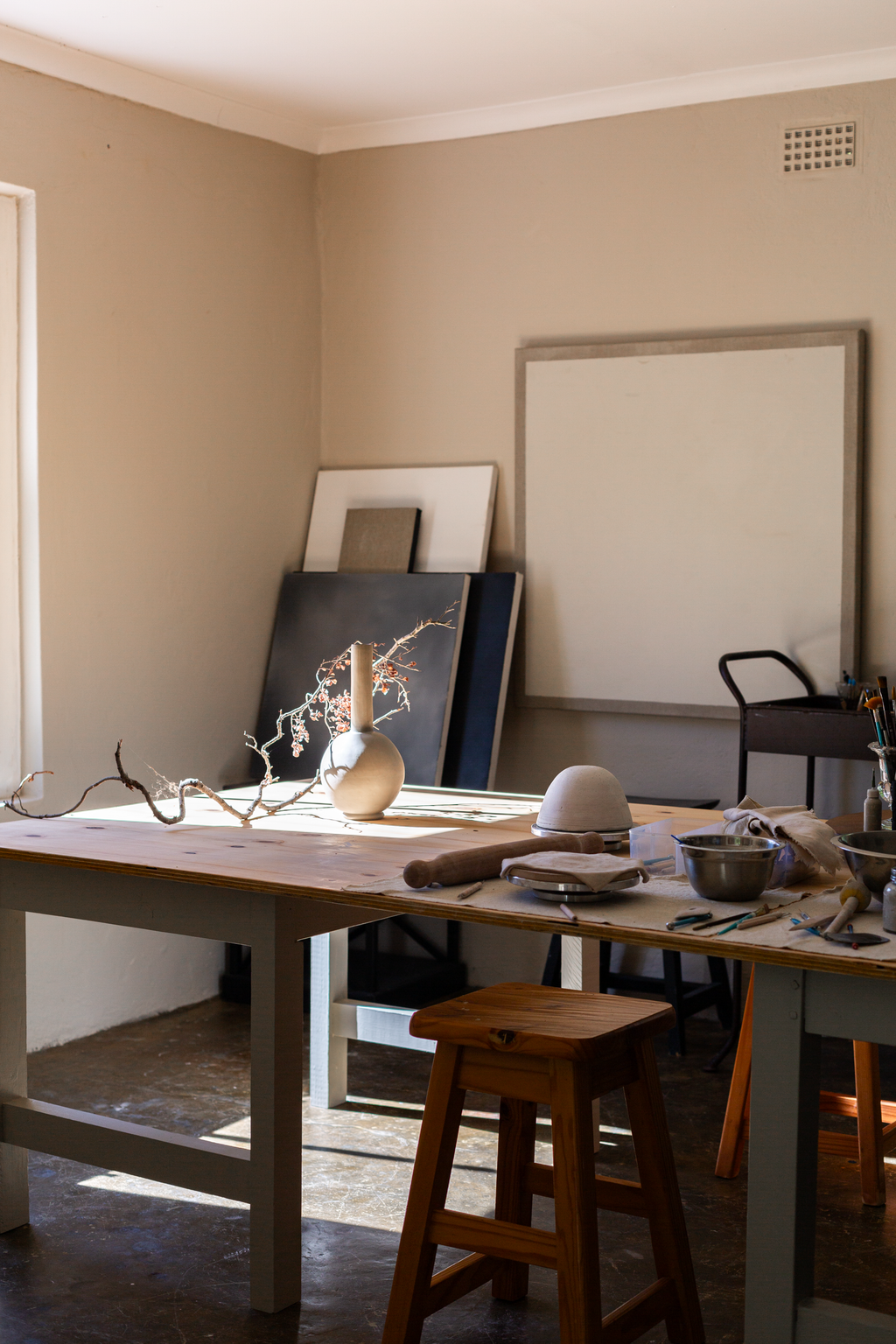 Studio with a table, stool, and various items on a beige wall.