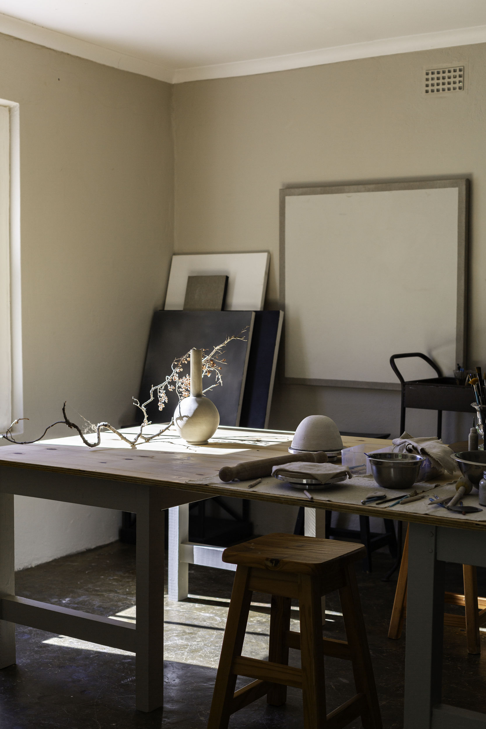Studio with a table, stool, and various items on a beige wall.